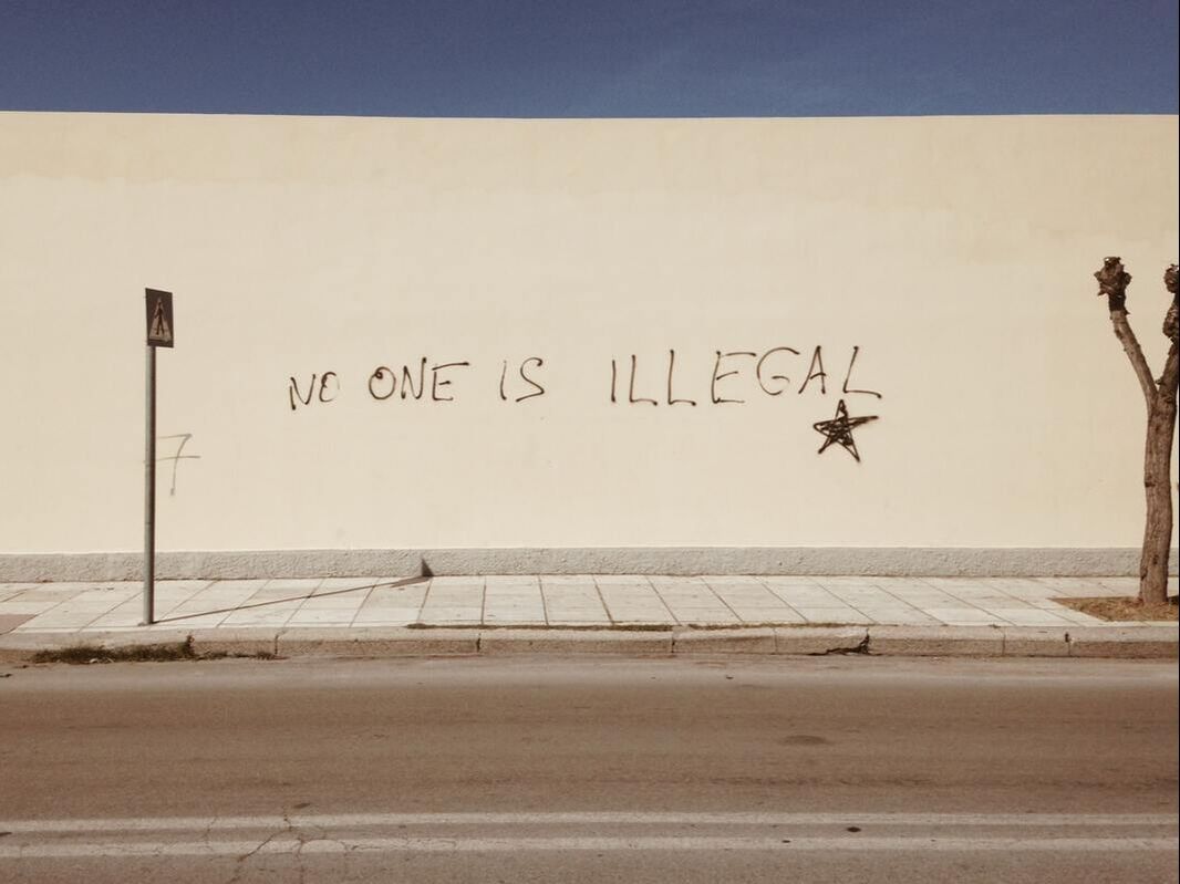 A wall with graffiti that reads 'no one is illegal'