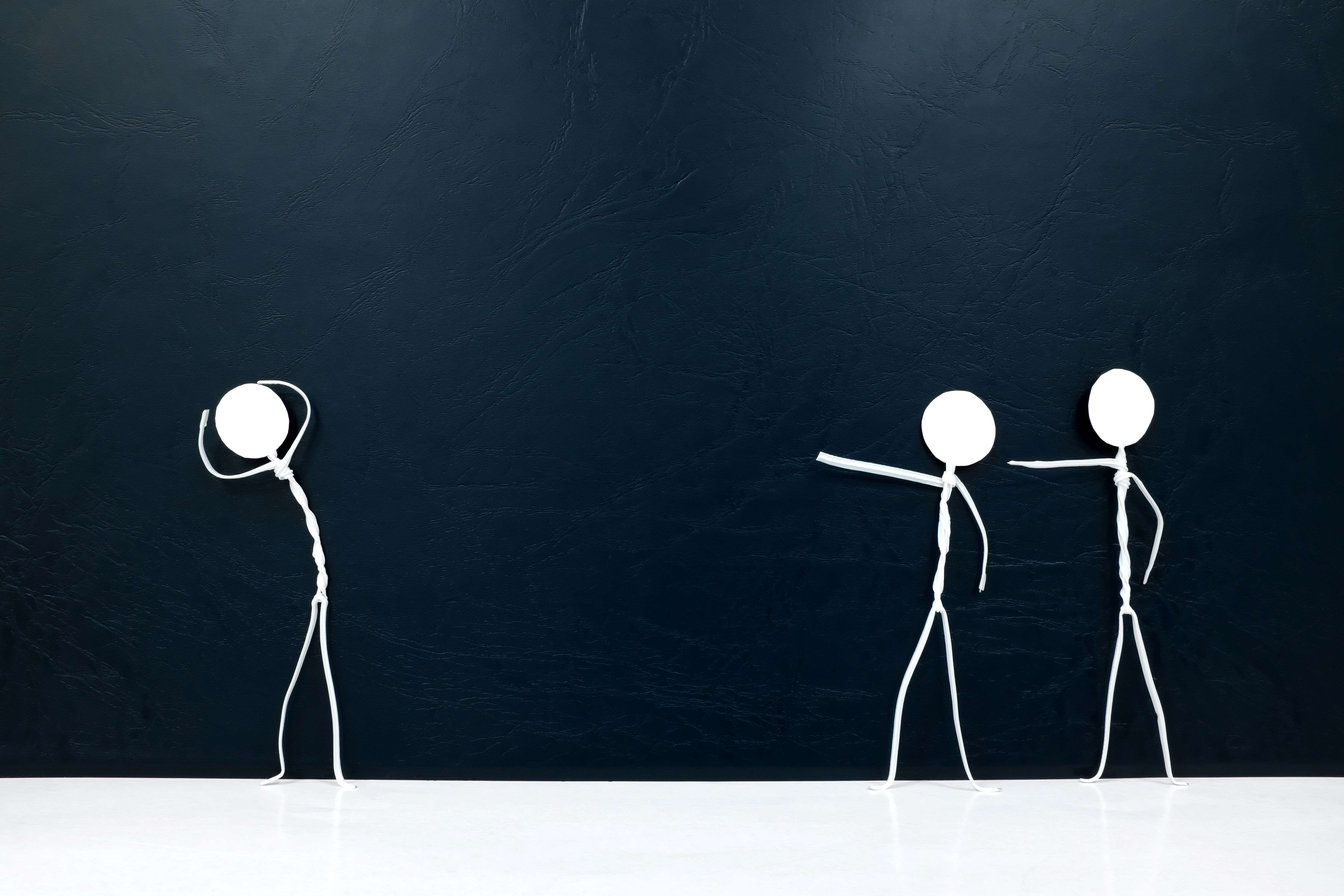 A drawing of 2 stick figures pointing at another one.